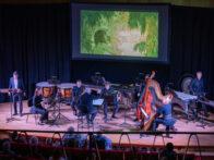 L'orchestre sur la scène devant l'écran de cinéma représentant une image de Moogli