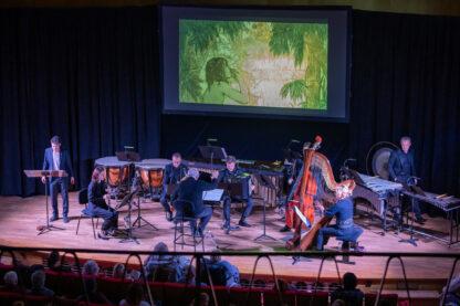 L'orchestre sur la scène devant l'écran de cinéma représentant une image de Moogli