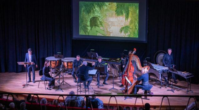 L'orchestre sur la scène devant l'écran de cinéma représentant une image de Moogli